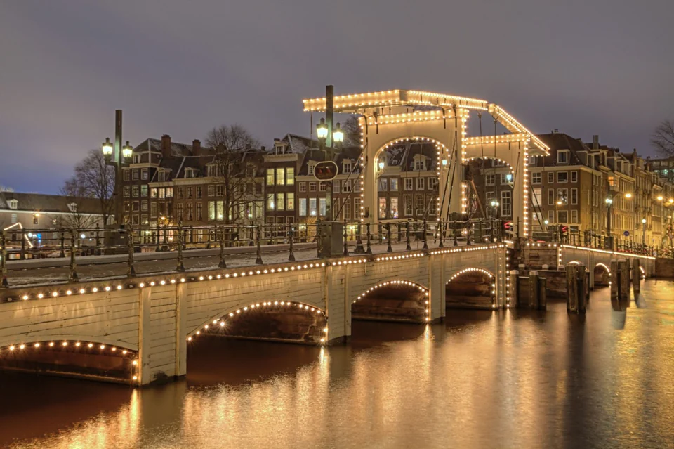 Beleuchtete Magere Brug über der Amstel in Amsterdam mit historischen Häusern am Ufer